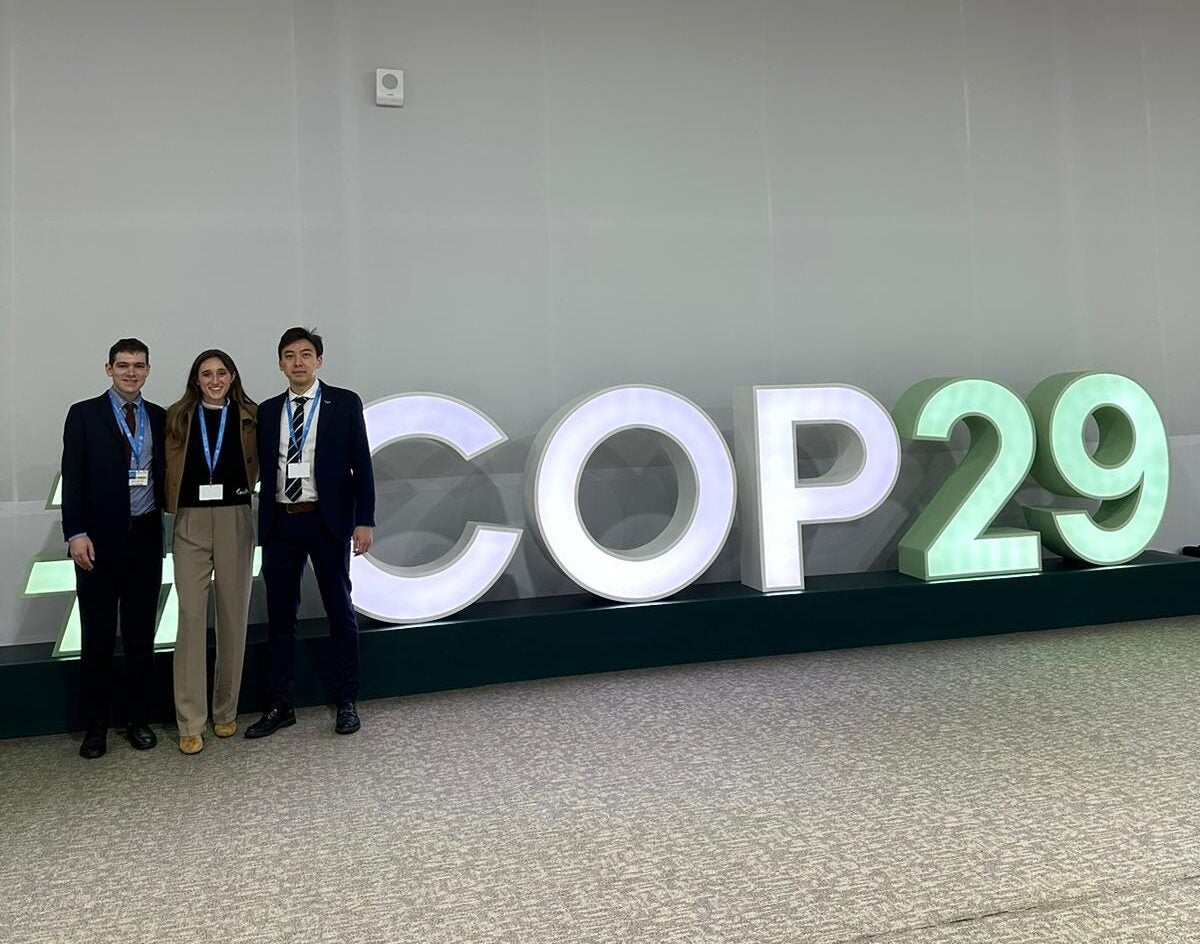 Zach Slotkin (MSFS'25), Anna Spear (MS-EIA'25) and Kamal Aubakirov (MSFS’25) pictured in front of the COP29 banner.